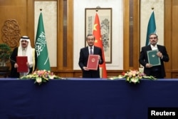 Top Chinese diplomat Wang Yi (center) holds up a March 10 deal in Beijing with Iran’s Supreme National Security Council Secretary Ali Shamkhani (right) and Saudi State Minister Musaad bin Muhammad al-Aiban.