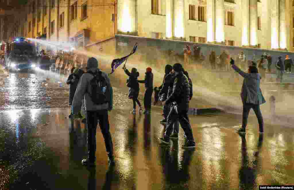 Protesters, one waving an EU flag, are sprayed by a water cannon.&nbsp;