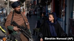 A Taliban security officer stands guard on a Kabul street as a woman passes by. (file photo)