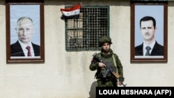 A Russian soldier stands between portraits of Syrian President Bashar al-Assad (right) and Russian President Vladimir Putin at a checkpoint on the outskirts of Damascus in 2018.