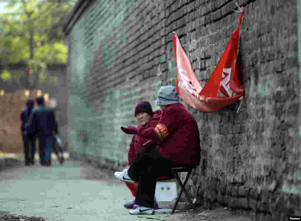 Elderly women with red armbands, identifying them as security volunteers, chat as they sit to watch over a traditional alleyway in central Beijing.