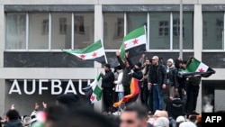 Syrians wave Syrian and German flags as they rally on December 8 in Berlin to celebrate the end of Bashar al-Assad's rule.