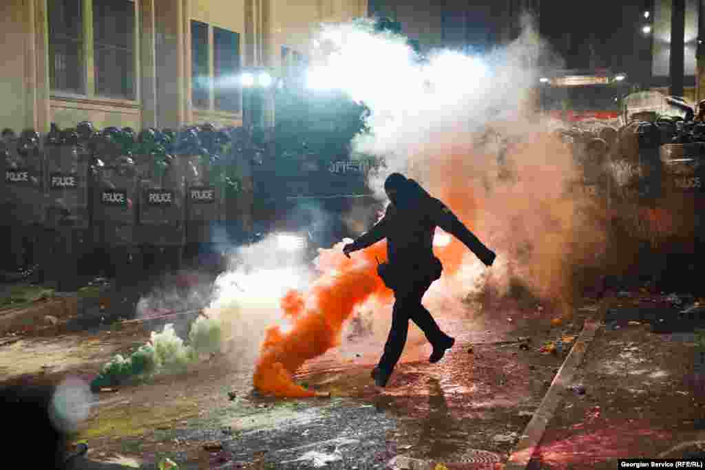  A masked police officer kicks a smoke bomb on November 29 during the second night of protests after the Georgian government announced the suspension of EU accession talks. &nbsp; 