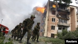 Georgian soldiers run past a building hit by a Russian air strike in Gori on August 9, 2008. 