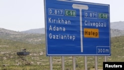 A Turkish soldier stands in a watchtower near a road sign showing directions to Cilvegozu border crossing and the Syrian city of Aleppo.