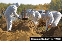 Cemetery workers in protective gear bury people who died of causes related to COVID-19 in Omsk on October 9.