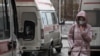 A woman wearing a protective face mask walks past ambulances outside a hospital in Omsk. 