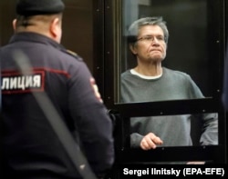 Former Russian Economic Development Minister Aleksei Ulyukayev stands inside a glass defendants' cage in a courtroom of the Moscow City Court in 2018.