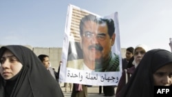 Protesters hold a poster depicting a montage of two faces, Sunni legislator Dhafer al-Ani and Saddam Hussein, and reads below: "Two faces of the same coin."