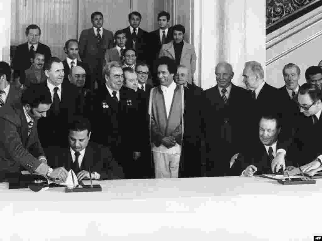 Qaddafi (center) and Soviet leader Leonid Brezhnev (to Qaddafi's right) smile as members of their delegations sign agreements during a visit to Moscow in December 1976.