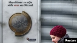 A pedestrian walks by a Eurobank advertisement featuring a 1-euro coin in Athens on February 8.