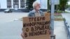 In a video grab from Severodvinsk TV, a man stands outside the city administration building on August 13, holding a cardboard sign demanding information about the accident in Nyonoksa.