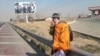 Mohammad Maleki, wearing a shawl that says "Let's Sweep Garbage," flashes the victory sign along a roadway outside the capital, where he and a colleague were dumped by security agents.