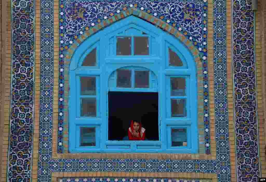 An Afghan girl looks out a window at Norouz festivities happening in the courtyard of the Hazrat-e-Ali Shrine in Mazar-e Sharif.