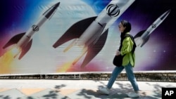 A woman walks past a banner showing missiles being launched in Tehran.